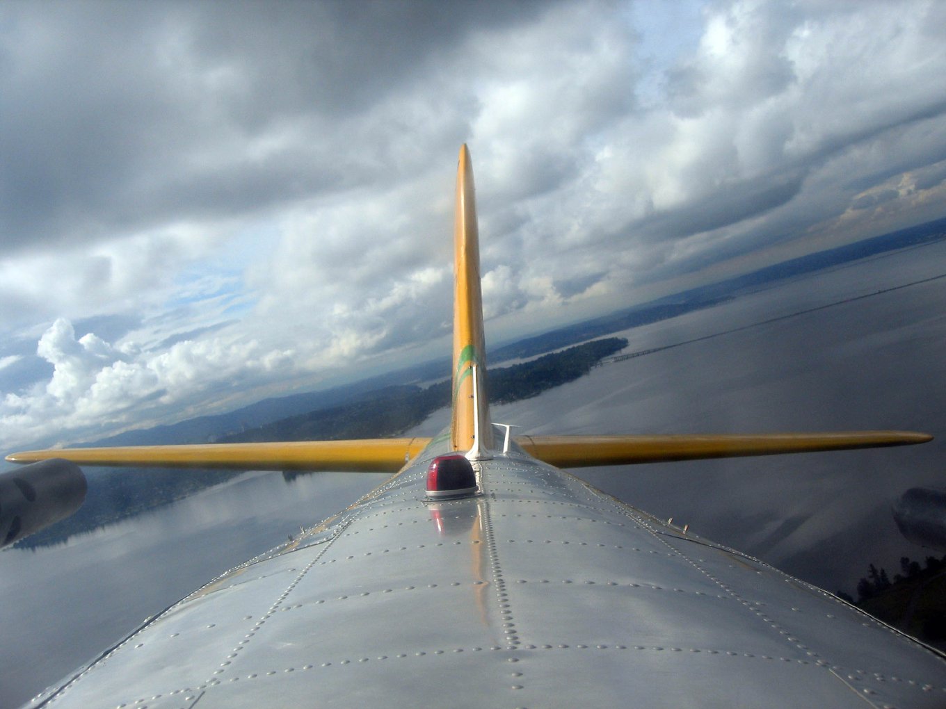 The B-17's tail fin seen from a dome on top of the fuselage, under clouds