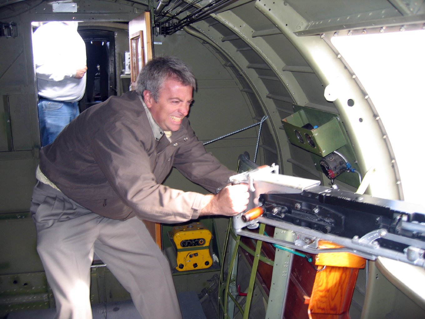 Brian aiming a waist machine gun out of an open window in the fuselage