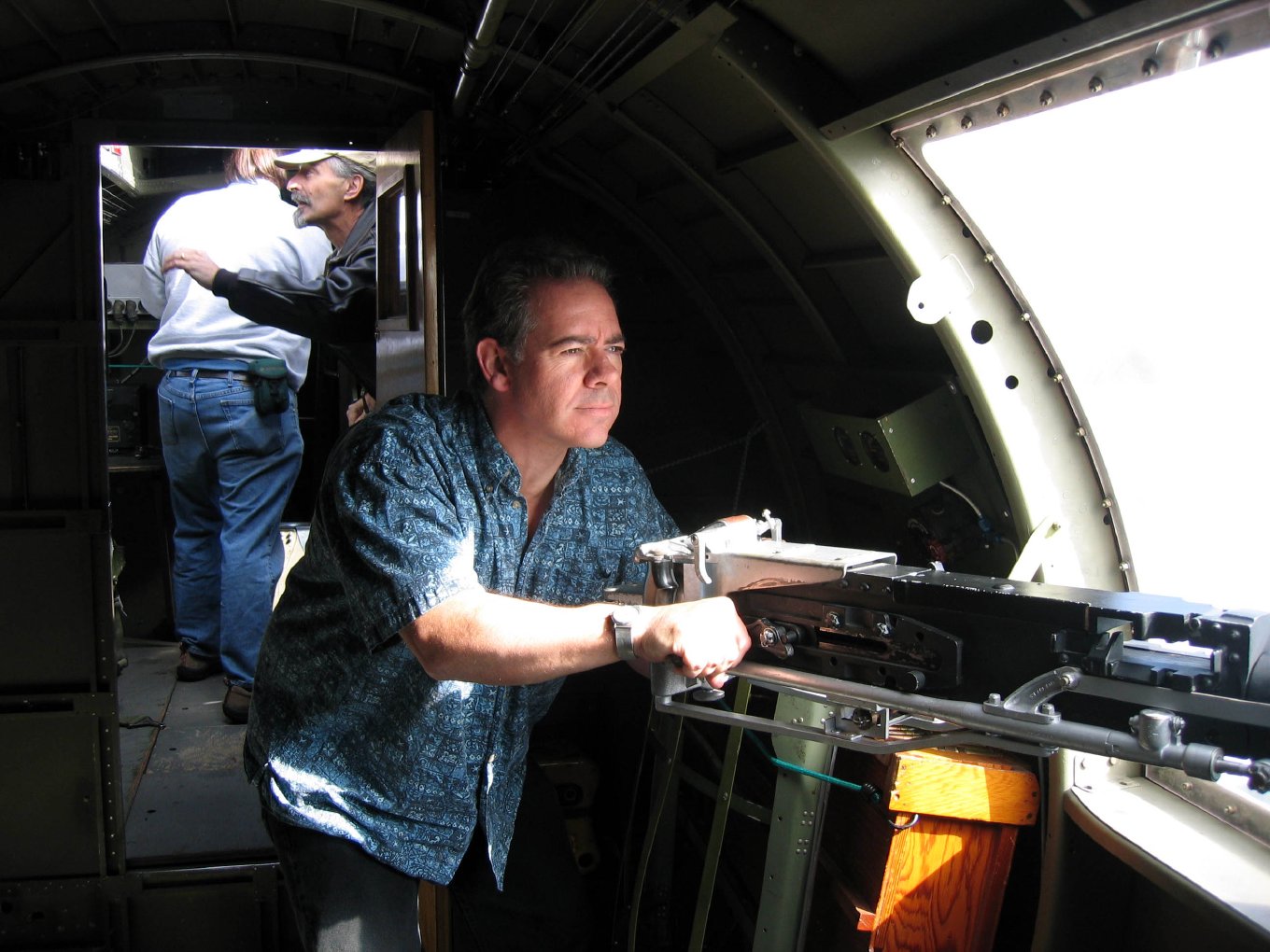 Mike aiming a waist machine gun out of an open window in the fuselage