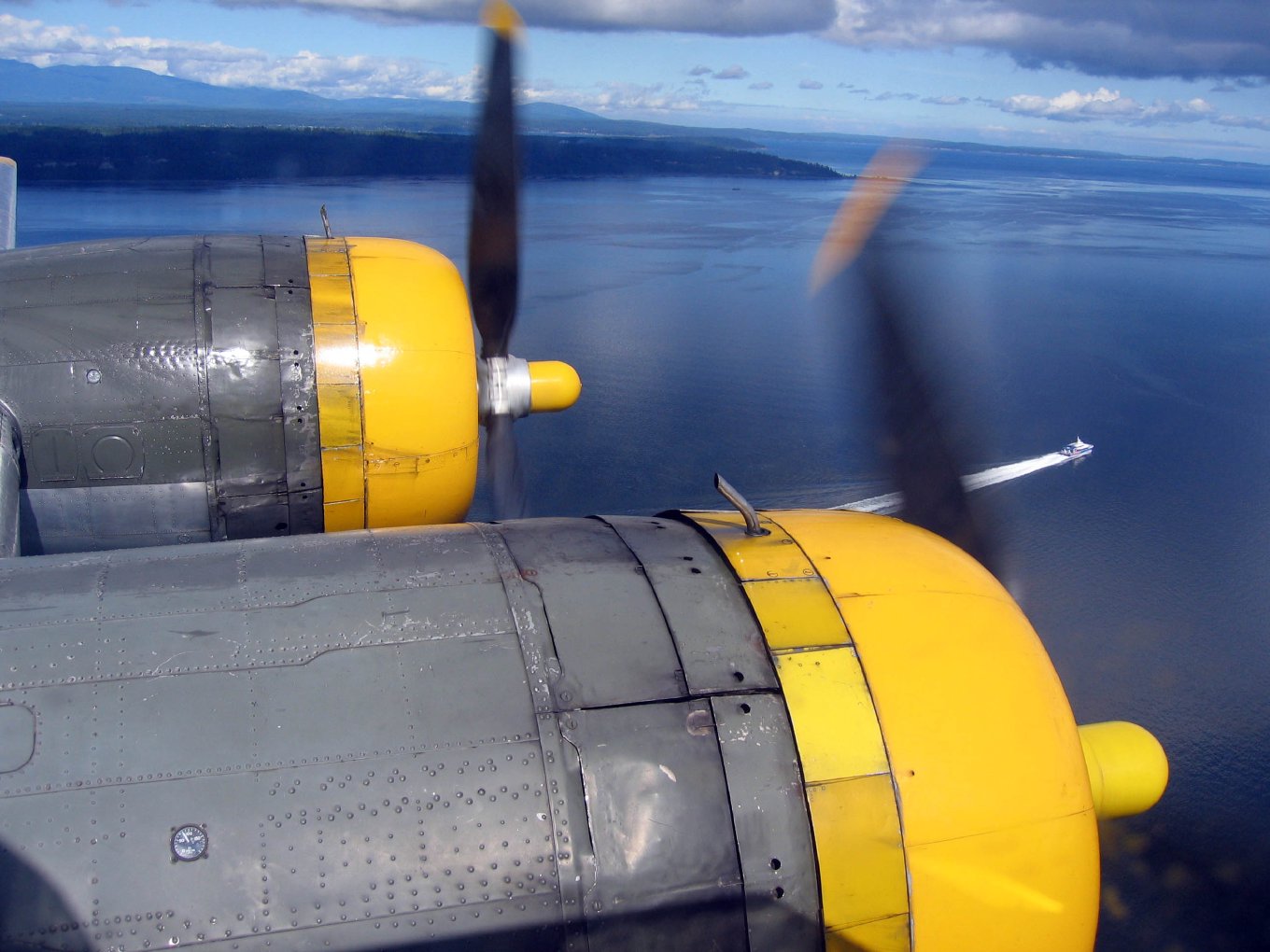 Two radial engines with yellow cowlings and spinning propellers, over the water