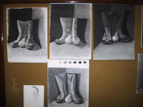 Four charcoal drawings of the boots and pear pinned up on a board