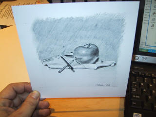 A hand holding a pencil drawing of the apple, cloth and pencils