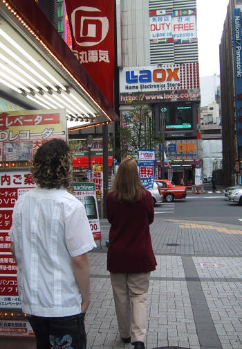 Chris and Deb on a sidewalk lined with electronics store signs