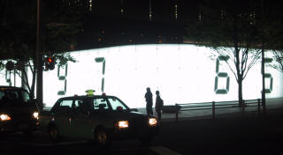A taxi passing a huge lit-up digital clock at night