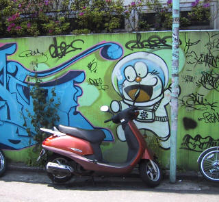 A red scooter parked in front of a graffiti wall featuring Doraemon