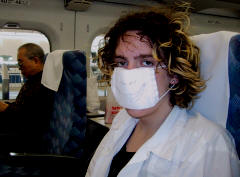 Chris wearing a white surgical mask in a train seat