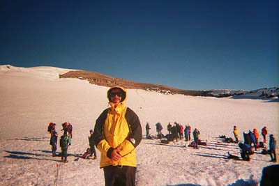 Mike in a yellow parka in the summit crater, with rope teams resting on the snow behind him