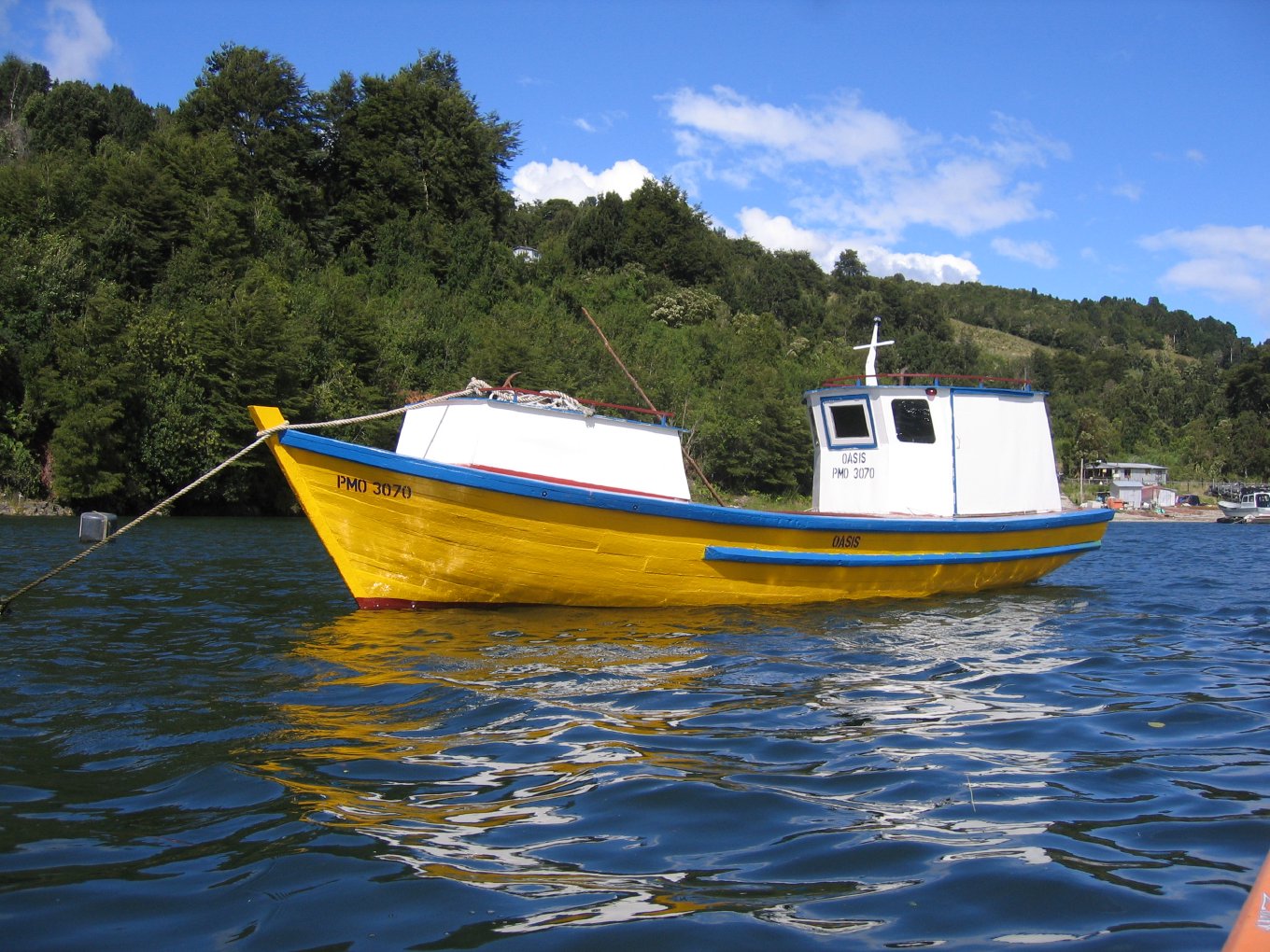 A yellow and white wooden fishing boat on blue water below green hills