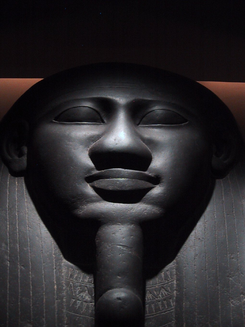 The carved black stone face on the lid of an Egyptian sarcophagus