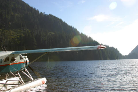 The floatplane's wing and float at the water's edge, looking west down the lake toward a gap in the mountains